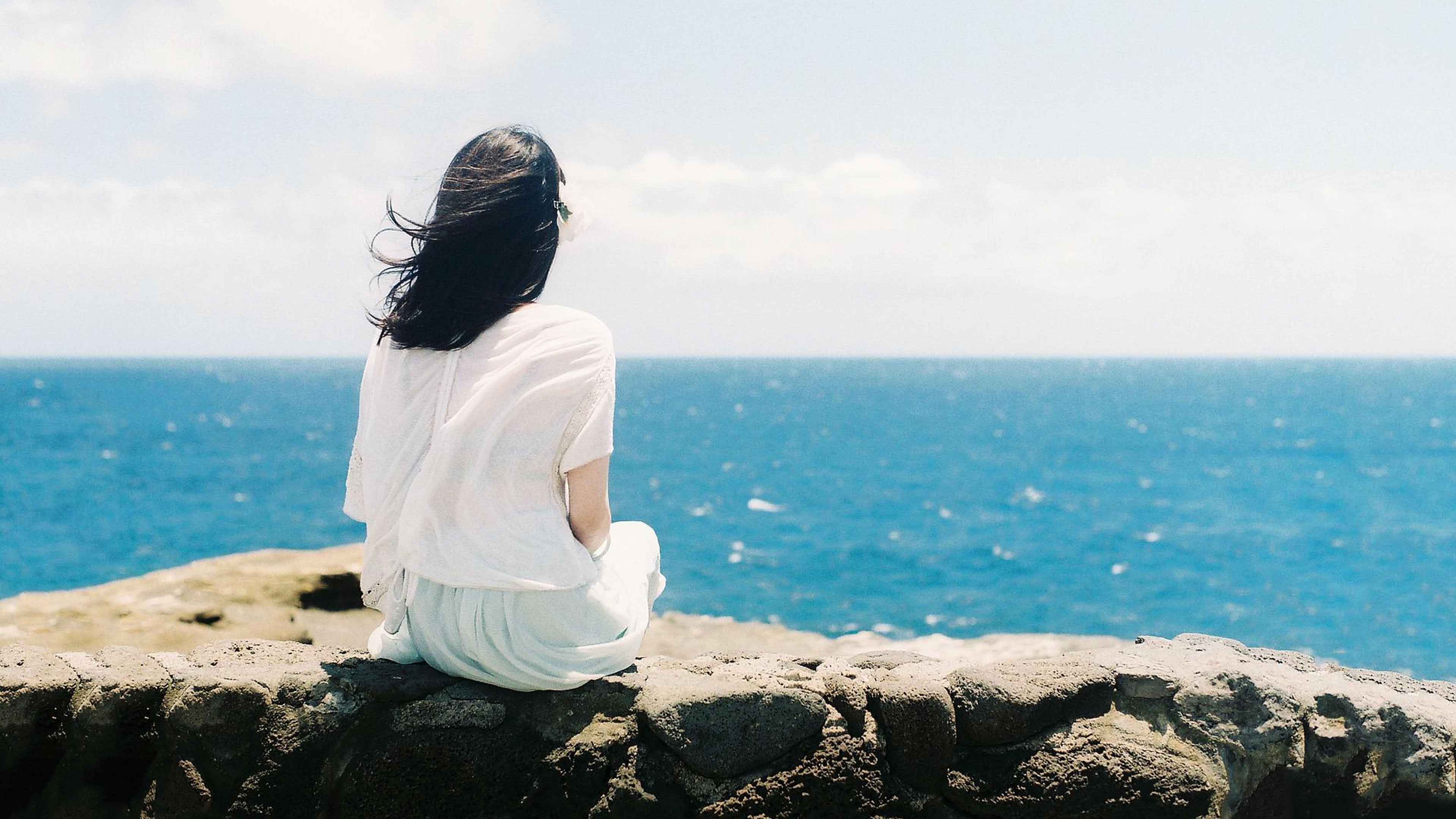 Hình ảnh một cô gái quay lưng lại trên một tảng đá hướng ra biển
