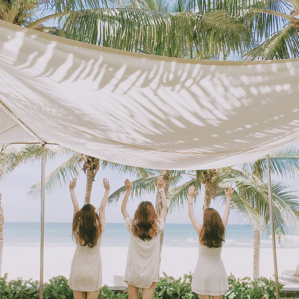 Hình ảnh ba cô gái quay lưng trên bãi biển dưới gốc cây dừa